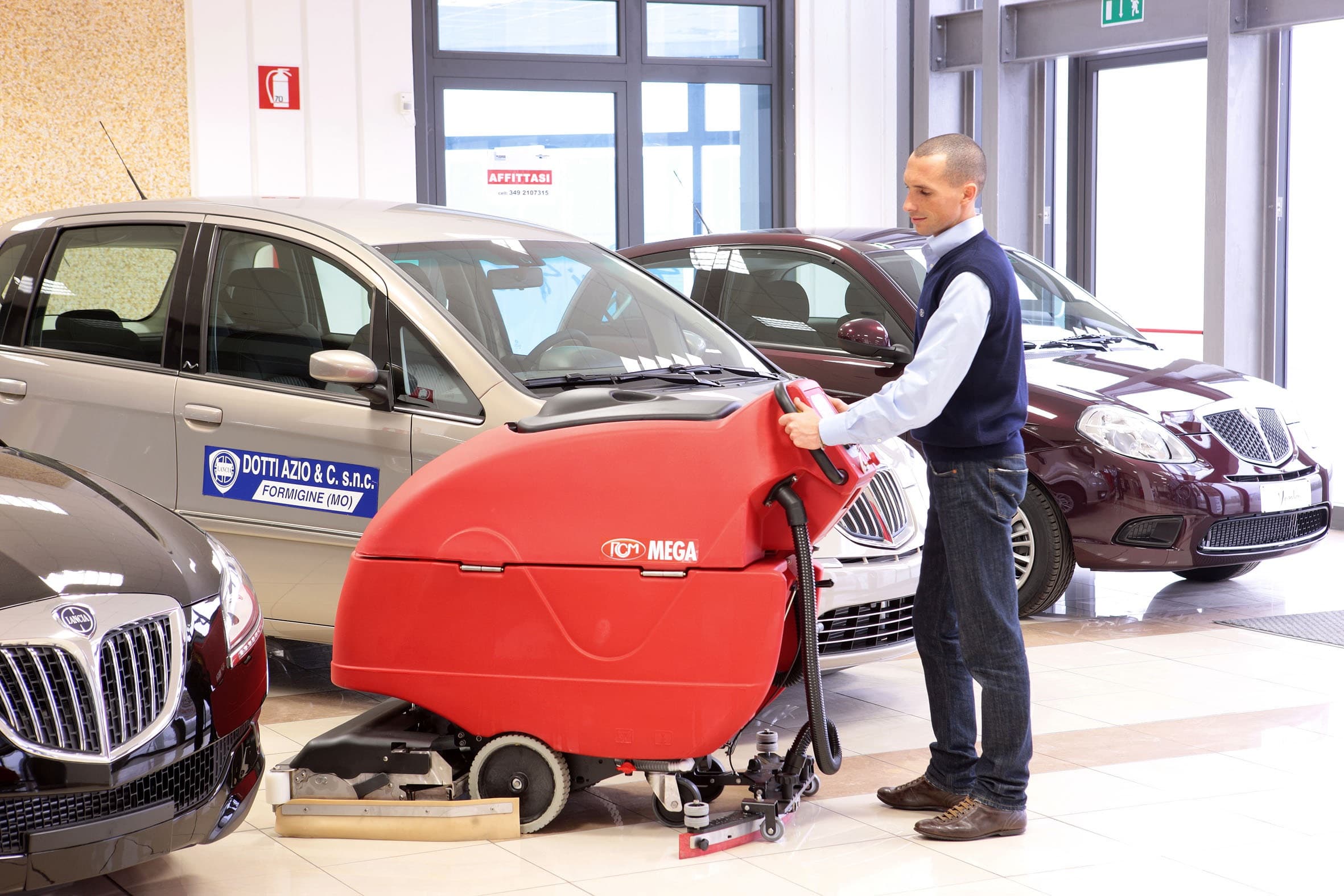 RCM MEGA Nachläufer-Scheuersaugmaschine zwischen Fahrzeugen in einem Autohaus-Showroom